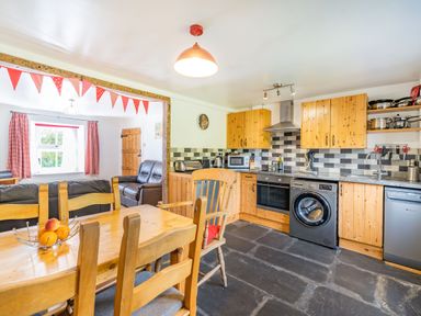 A kitchen with wooden cabinets a dining table with chairs and a living area with leather sofas at No 7 Spark Bridge near Ulverston