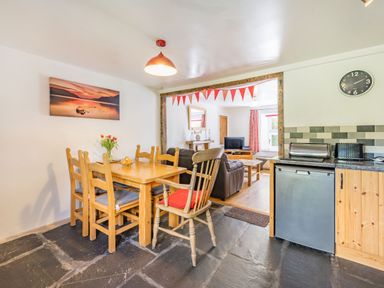 A dining area with a wooden table and chairs next to a kitchen with a small fridge and a living room with a television at No 7 Spark Bridge near Ulverston