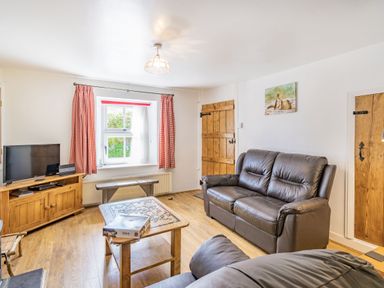 A living room with leather sofas a wooden coffee table a television on a cabinet and red check curtains at No 7 Spark Bridge near Ulverston