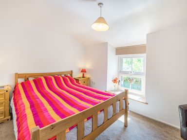 A bedroom with a wooden bed with a striped pink orange and red blanket and bedside tables with lamps at No 7 Spark Bridge near Ulverston