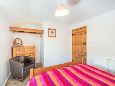 A bedroom with a wooden door a wooden chest of drawers with a mirror a black chair and a bed with a colorful striped blanket at No 7 Spark Bridge near Ulverston