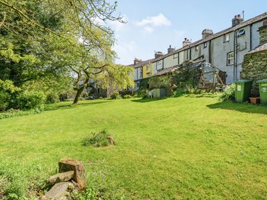A grassy backyard with a tree a stone shed garden furniture and terraced houses at No 7 Spark Bridge near Ulverston