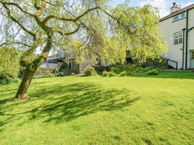 A green garden with a large tree and stone buildings in the background at No 7 Spark Bridge near Ulverston
