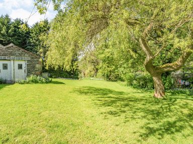 A garden with a large tree on the right and a stone shed with white doors on the left at No 7 Spark Bridge near Ulverston