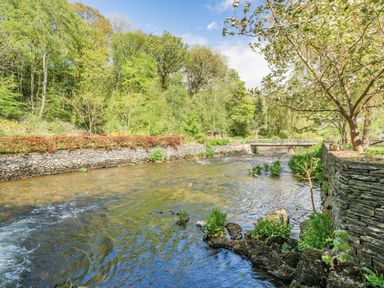 A river flowing through a wooded area with stone walls on both sides at No 7 Spark Bridge near Ulverston