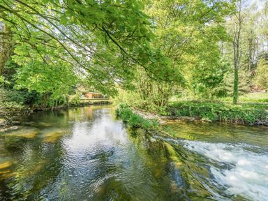 A river with flowing water surrounded by trees and greenery at No 7 in Spark Bridge near Ulverston