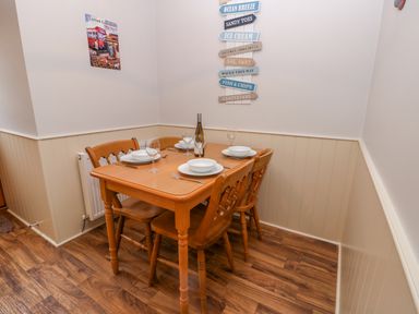 A dining area with a wooden table set for four with plates and wine glasses at Little Venice Whitby