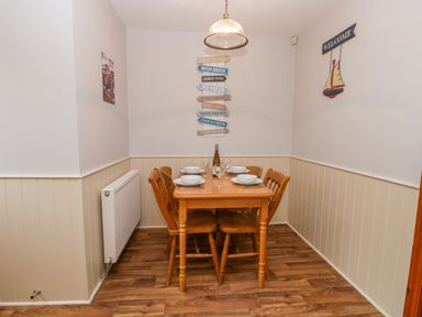 A dining area with a wooden table set for four with plates wine glasses and a bottle on top at Little Venice in Whitby