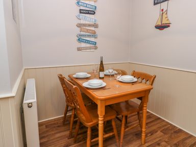 A dining area with a wooden table set for four with plates bowls wine glasses and a wine bottle on a wood floor at Little Venice in Whitby