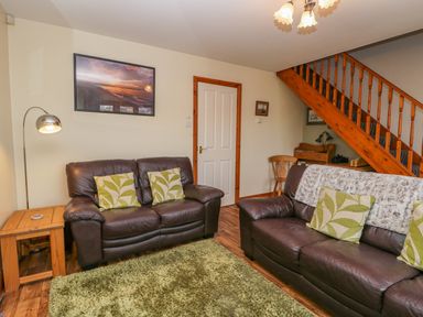 A living room with two brown leather sofas with green patterned cushions and a green rug at Little Venice in Whitby
