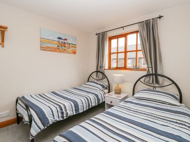 A bedroom with two single beds with striped bedding a nightstand lamp window and painting at Little Venice in Whitby