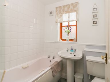 A bathroom with a bathtub sink toilet window with floral blind and a vase with flowers at Little Venice in Whitby