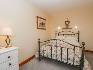 A bedroom with a metal bed frame with floral bedding a white dresser with a lamp a picture on the wall and a heart-shaped wreath above the bed at Little Venice in Whitby