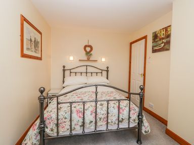 A bedroom with a metal bed frame floral bedspread white pillows bedside table paintings and a door at Little Venice in Whitby