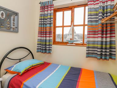 A bedroom with a single bed with a colorful striped duvet and pillow next to a window with striped curtains a model sailboat on the windowsill and a framed display of knots on the wall at Little Venice in Whitby