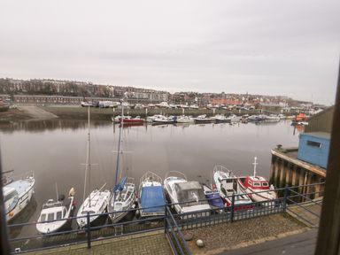 A marina with multiple boats docked along a river and buildings in the background at Little Venice in Whitby