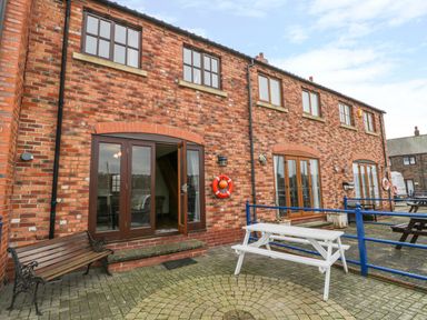 A brick building with multiple windows doors a white picnic table and a wooden bench outside at Little Venice in Whitby