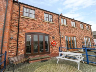 A brick building exterior with multiple windows and doors a bench and a white picnic table at Little Venice in Whitby