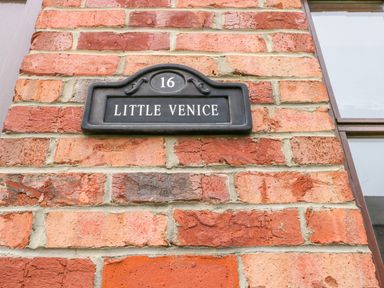 A black house number plaque with number 16 and name Little Venice on a red brick wall next to a window at Little Venice in Whitby