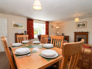 A dining area with a wooden table set with white dishes and cutlery in a living room with red curtains and a fireplace at Moorside in Horrabridge near Tavistock