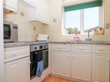 A kitchen with white cabinets a stove microwave toaster and a window at Moorside Horrabridge near Tavistock