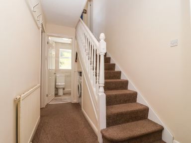 A hallway with carpeted stairs leading up and a door open to a bathroom showing a toilet at Moorside Horrabridge near Tavistock