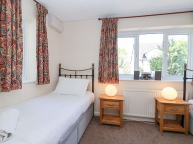 A bedroom with two single beds wooden bedside tables with lamps and windows with patterned curtains at Moorside Horrabridge near Tavistock