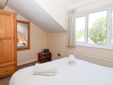 A bedroom with a bed with towels on it a wooden wardrobe a mirror and a window at Moorside in Horrabridge near Tavistock