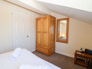 A bedroom with a wooden wardrobe a mirror on the wall a bed with rolled towels and a small table with a phone and speaker at Moorside in Horrabridge near Tavistock