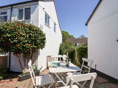 An outdoor patio area with a white table and chairs a bottle of wine and two glasses on the table surrounded by white buildings and greenery at Moorside in Horrabridge near Tavistock