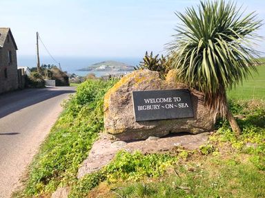 A road leading to a coastal area with a stone sign that says welcome to Bigbury on Sea near Modbury
