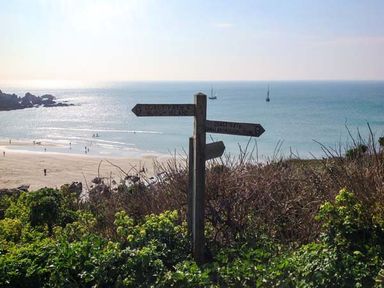 A wooden signpost on a coastal path overlooking the beach and sea with sailboats at Quarterdeck in Bigbury-on-Sea near Modbury