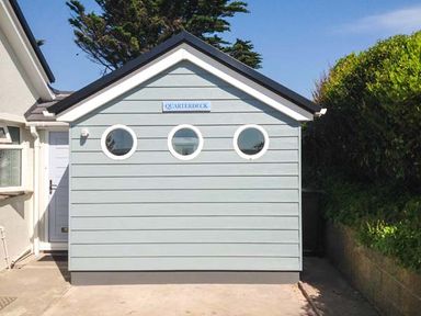 The exterior of a building with three round windows and a sign that says Quarterdeck at Bigbury-on-Sea near Modbury