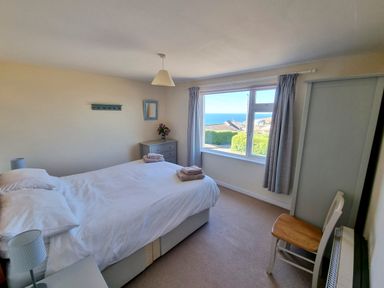 A bedroom with a double bed a chair and a window showing a sea view at Quarterdeck in Bigbury-on-Sea near Modbury