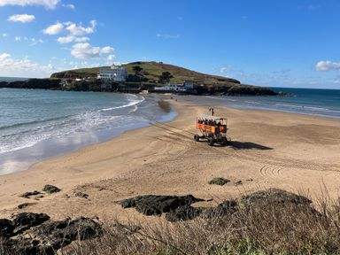 A sandy beach with a group of people on an orange raised vehicle near the shoreline at Quarterdeck in Bigbury-on-Sea near Modbury
