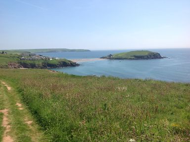 A coastal landscape with grassy cliffs houses and a small island at Quarterdeck in Bigbury-on-Sea near Modbury