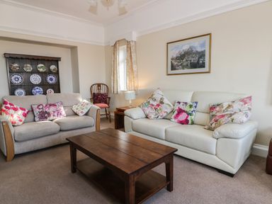 A living room with two sofas with floral cushions a wooden coffee table a wooden chair a display cabinet with plates and a framed picture on the wall at Seascape in Bridlington