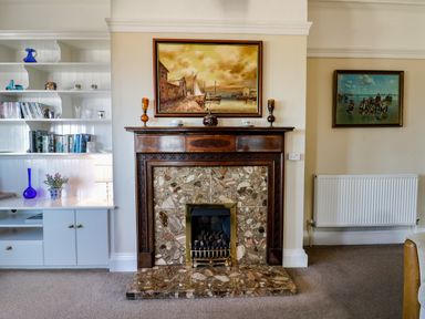 A tiled fireplace with a dark wood mantel and paintings above in a living room with built in shelves at Seascape Bridlington