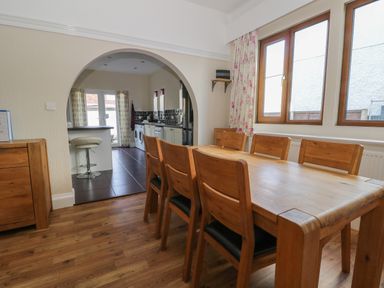 A dining room with wooden table and chairs near windows and an archway leading to a kitchen with appliances at Seascape in Bridlington