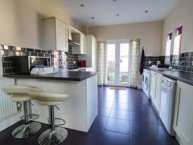A kitchen with black countertops white cabinets two bar stools and glass doors leading outside at Seascape in Bridlington