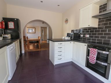 A kitchen with white cabinets black countertops black tiled backsplash and a dining table visible through an arch at Seascape in Bridlington