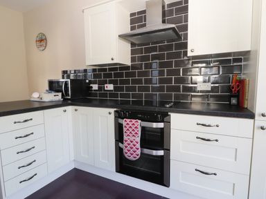 A kitchen with white cabinets a black countertop a black oven a microwave and black subway tile backsplash at Seascape in Bridlington