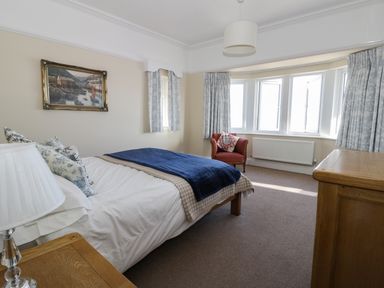 A bedroom with a bed, wooden furniture, an armchair, and windows with curtains at Seascape in Bridlington