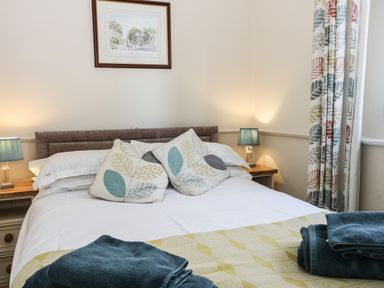A bedroom with a bed featuring patterned pillows bedside tables with lamps and patterned curtains at Seascape Bridlington