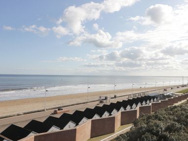 A beach with a row of black roofed beach huts and a promenade at Seascape in Bridlington