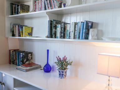 White shelves with books a blue vase a potted plant and a lamp on a white surface at Seascape Bridlington