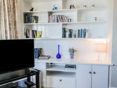 A white shelving unit with books dvds a blue vase a plant and a lamp next to a television in a living room at Seascape in Bridlington
