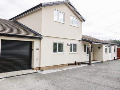 The exterior of a two story house with a garage and multiple windows at Bryn Derw Holiday Cottage in Eglwysbach near Llanrwst and Conwy