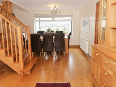 A dining room with wooden floor leather chairs a wooden staircase and wooden cabinets at Bryn Derw Holiday Cottage in Eglwysbach near Llanrwst and Conwy