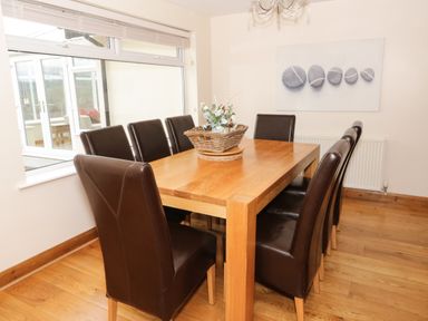 A dining room with a wooden table surrounded by eight brown leather chairs and a basket with flowers on the table at Bryn Derw Holiday Cottage in Eglwysbach near Llanrwst and Conwy